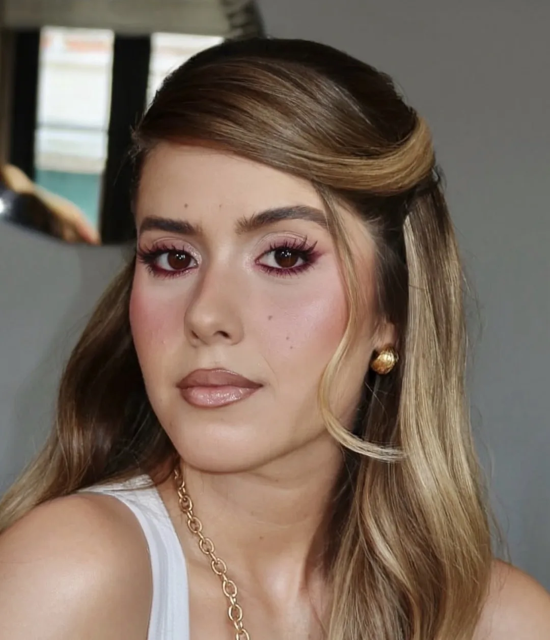 Maquilhagem com eyeliner bordeaux, pele luminosa e cabelo meio apanhado, fotografada com luz natural de janela