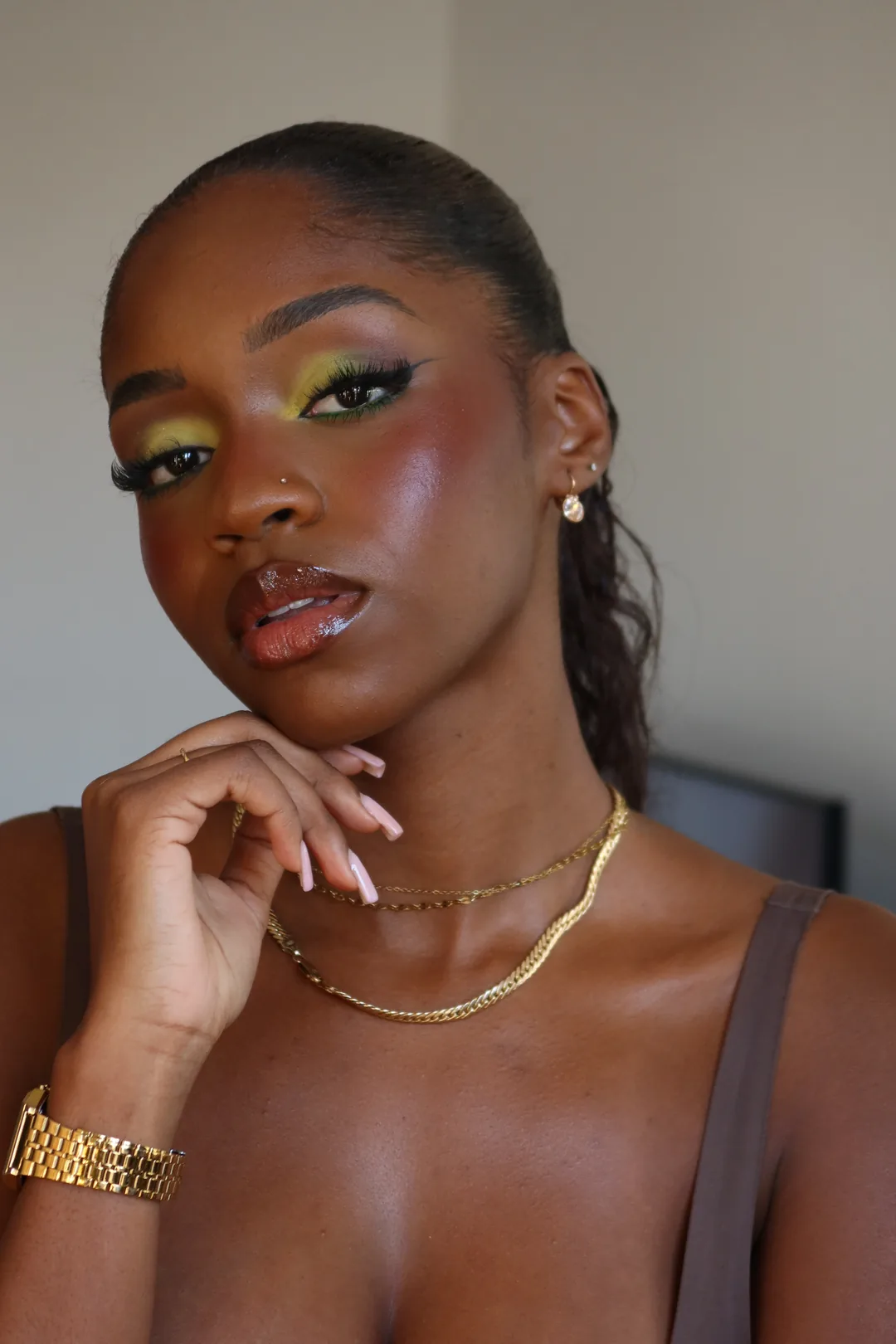 Deep skin with bright yellow and green eyeshadow, glowing skin and gold jewellery